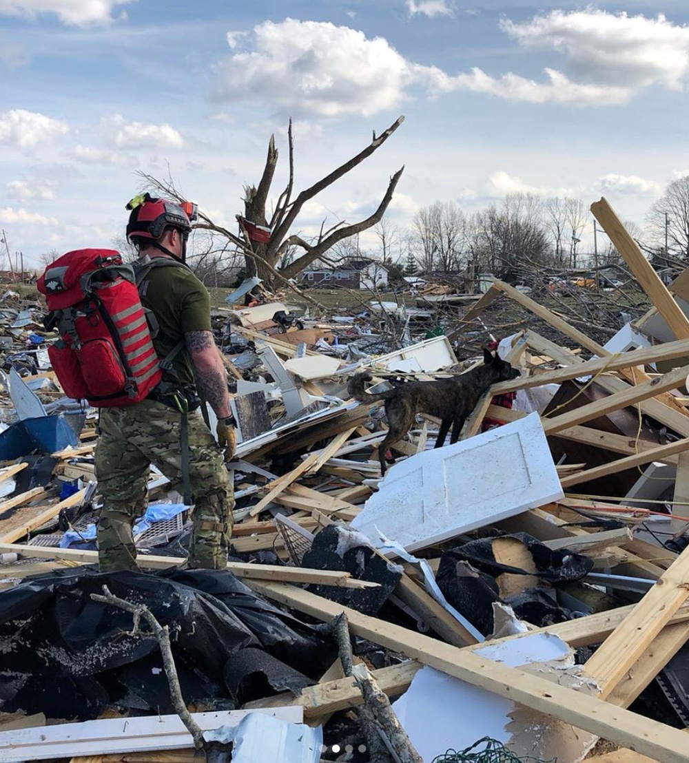 Search and rescue operator with K-9 unit conducting operations in tornado debris